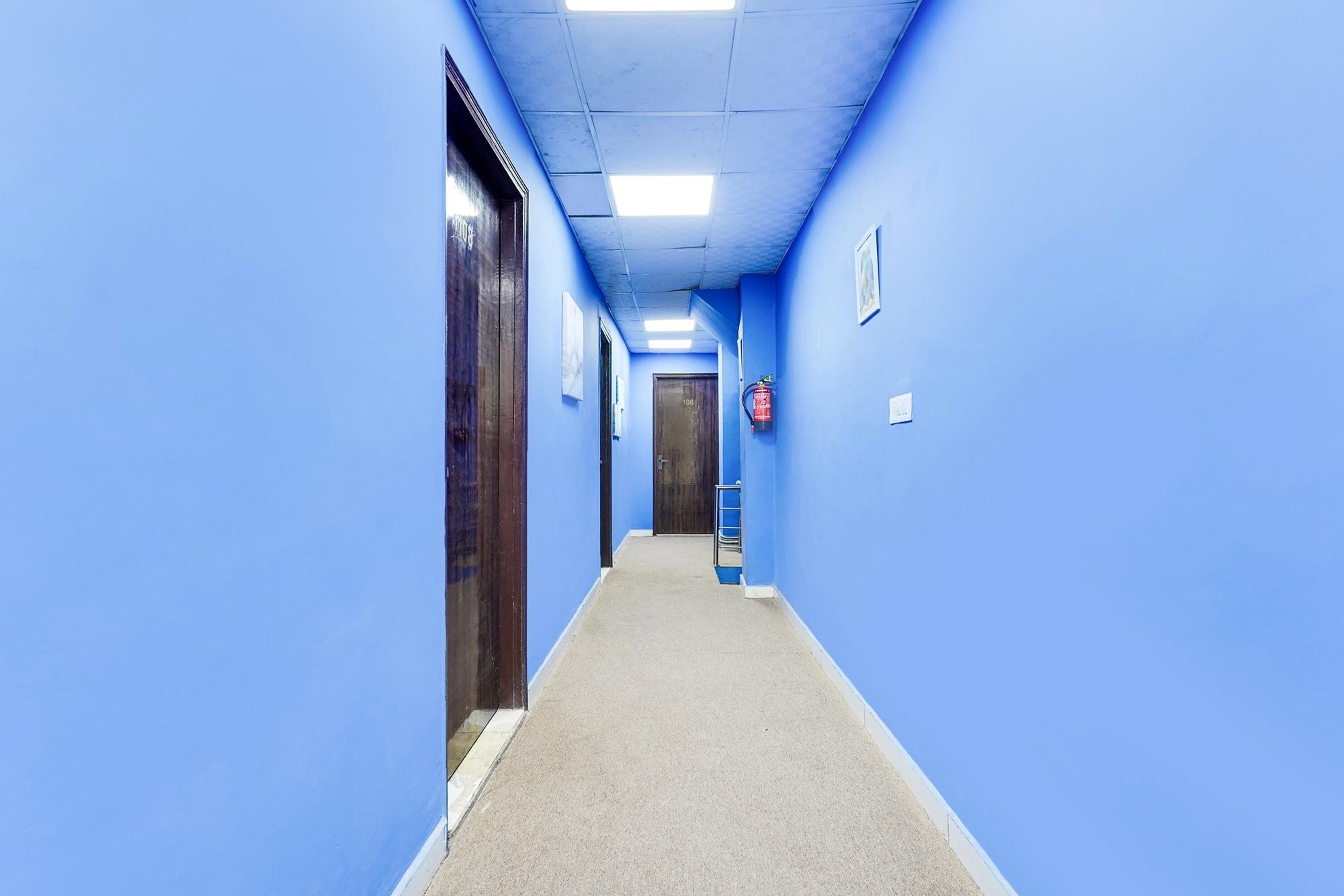 A narrow hallway with blue walls and a carpeted floor, leading to a door at the end.