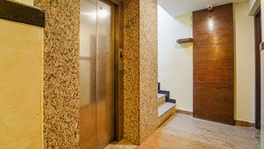 An interior hallway with a granite wall, a wooden door, and a staircase leading to another floor. - FabHotel HR Residency (Coimbatore)