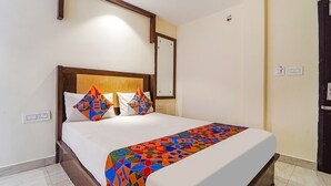 A neatly made bed with a colorful geometric-patterned bedspread, a wooden headboard, and a small bedside table with a lamp. - FabHotel HR Residency (Coimbatore)