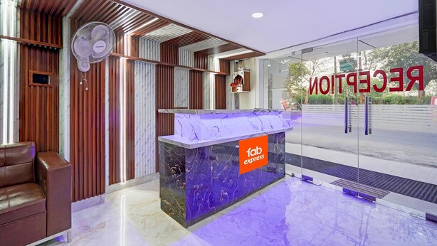A reception desk with a marble top and a 'fab express' sign, a brown leather sofa, and a wall-mounted fan. - FabExpress Miss Too (Noida)