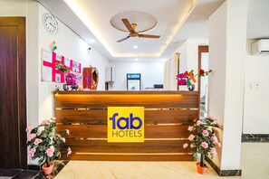A hotel reception area with a wooden reception desk, a ceiling fan, and potted plants. - FabHotel Vishal Palace (Agra)