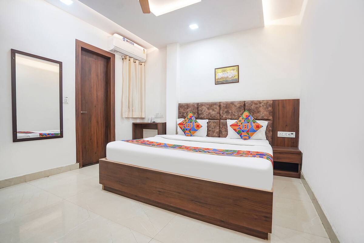 A bedroom with a wooden bed frame, a nightstand, a mirror, and an air conditioning unit.