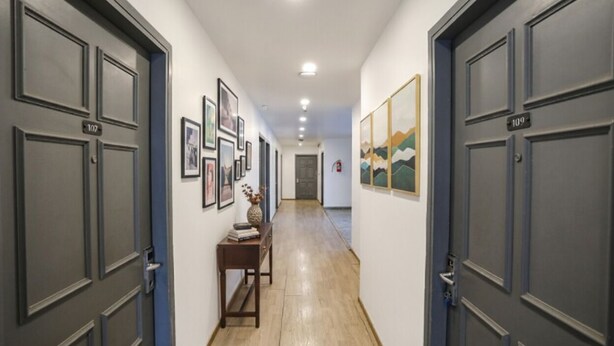 A hallway with dark grey doors, numbered 107 and 109, leading to rooms. There are framed pictures on the walls and a small table with a vase and books.