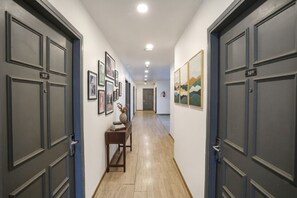 Un pasillo con puertas de color gris oscuro, con los números 107 y 109, que conducen a habitaciones. En las paredes hay cuadros enmarcados y una pequeña mesa con un jarrón y libros.