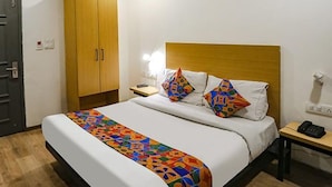 A hotel room with a bed, a wooden wardrobe, a bedside table with a lamp, and a telephone.