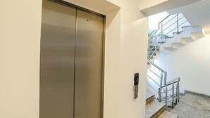 A modern elevator with a metallic finish, a stairwell with metal railings, and a concrete floor.