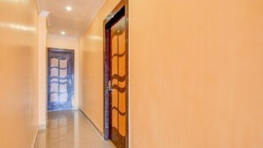 A hallway with a wooden door with a geometric pattern, a tiled floor, and a plain wall. - FabHotel Dreamz Heaven (Barasat)