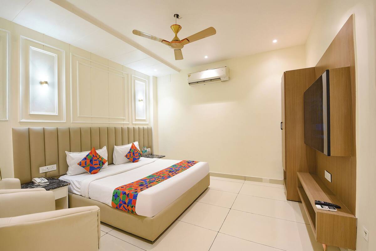 Una habitación de hotel con cama, mesita de noche, silla, televisión y ventilador de techo.