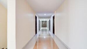 A long, narrow hallway with a polished floor and white walls. - FabHotel Leo Grand (Anekal)