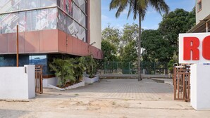 A building with a large red 'R' sign, a gated entrance, and a paved area with plants and a fence. - FabHotel Leo Grand (Anekal)