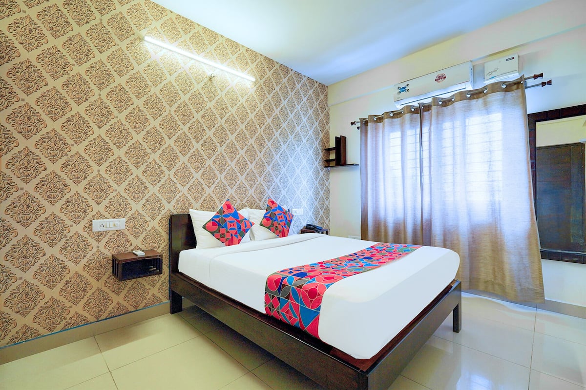 A neatly made bed with a patterned bedspread, a bedside table with a lamp, and a wall-mounted air conditioning unit.