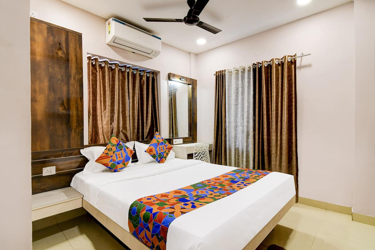A hotel room with a bed, a ceiling fan, an air conditioning unit, a desk, and curtains.