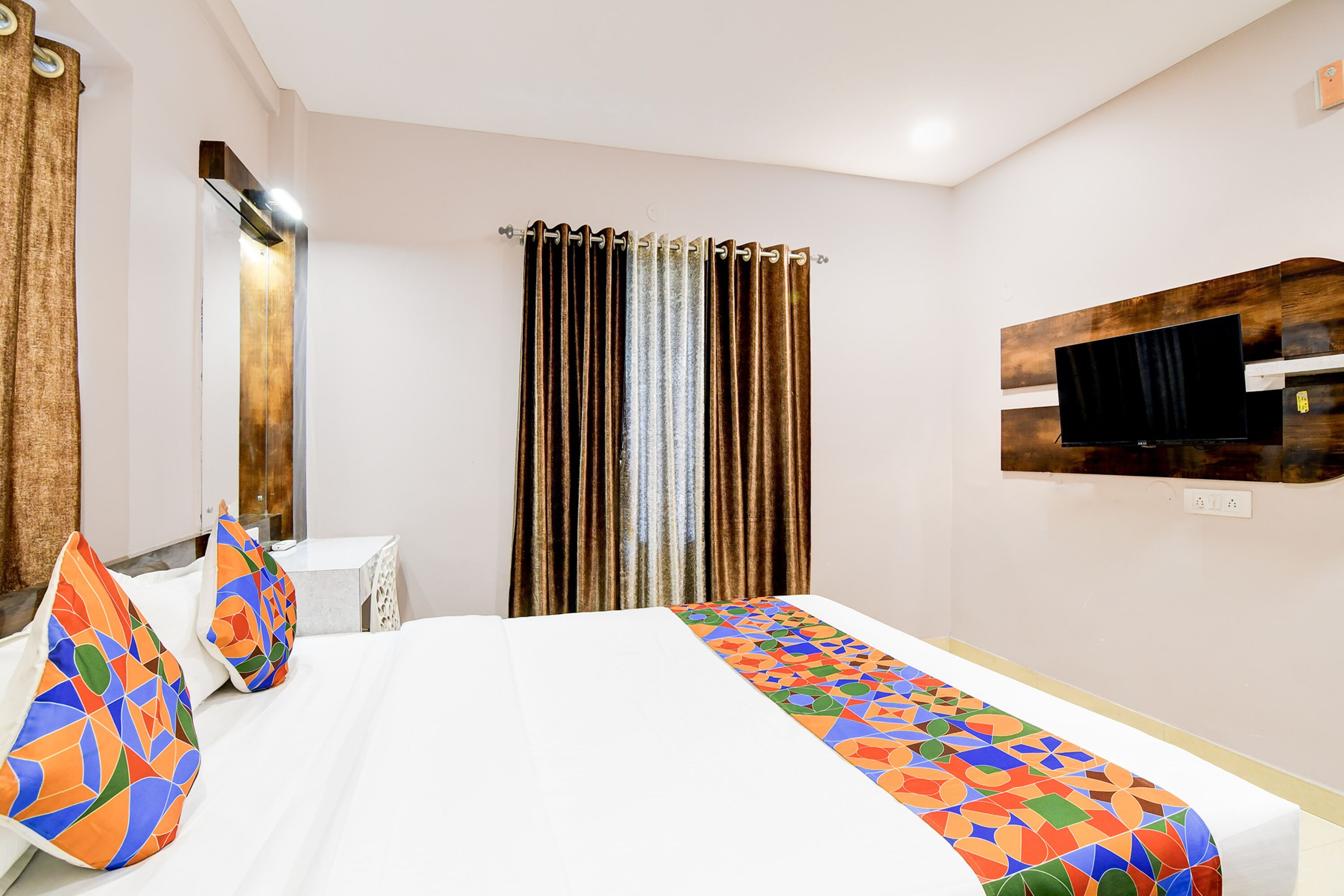 A hotel room with a bed, a TV mounted on the wall, and curtains.