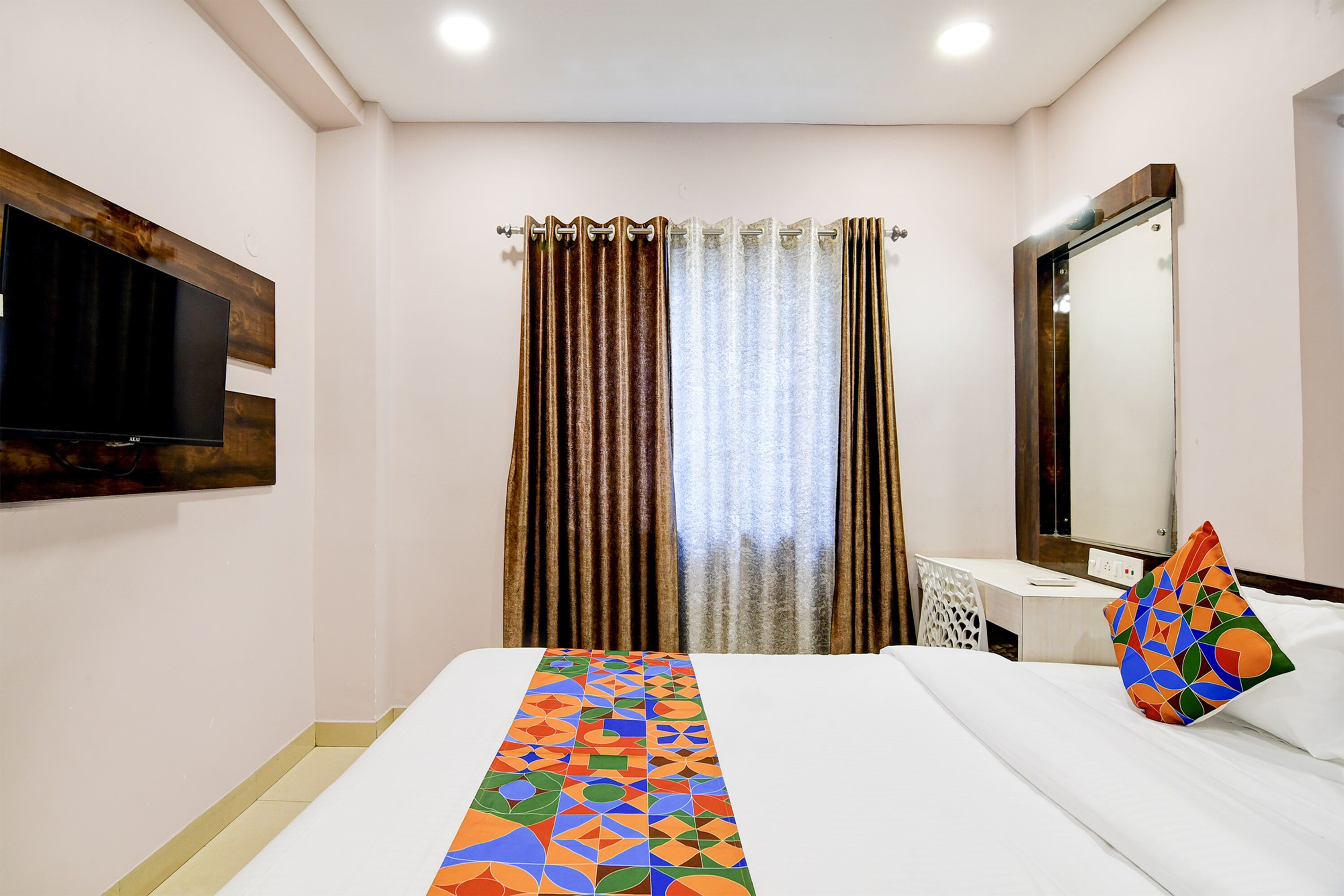A hotel room with a bed, a TV mounted on the wall, a desk, and a mirror.