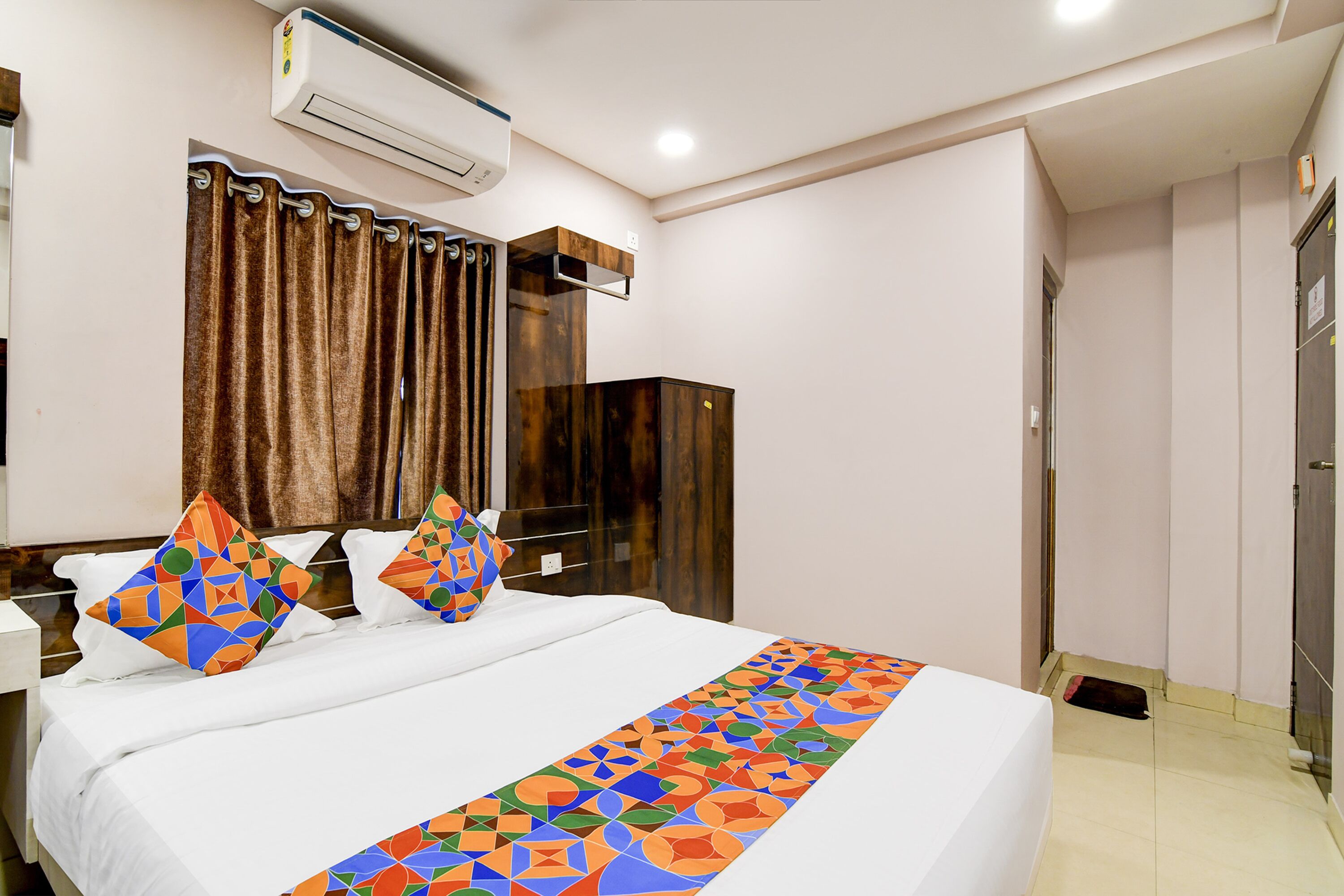 A hotel room with a bed, a wardrobe, an air conditioning unit, and a curtain.