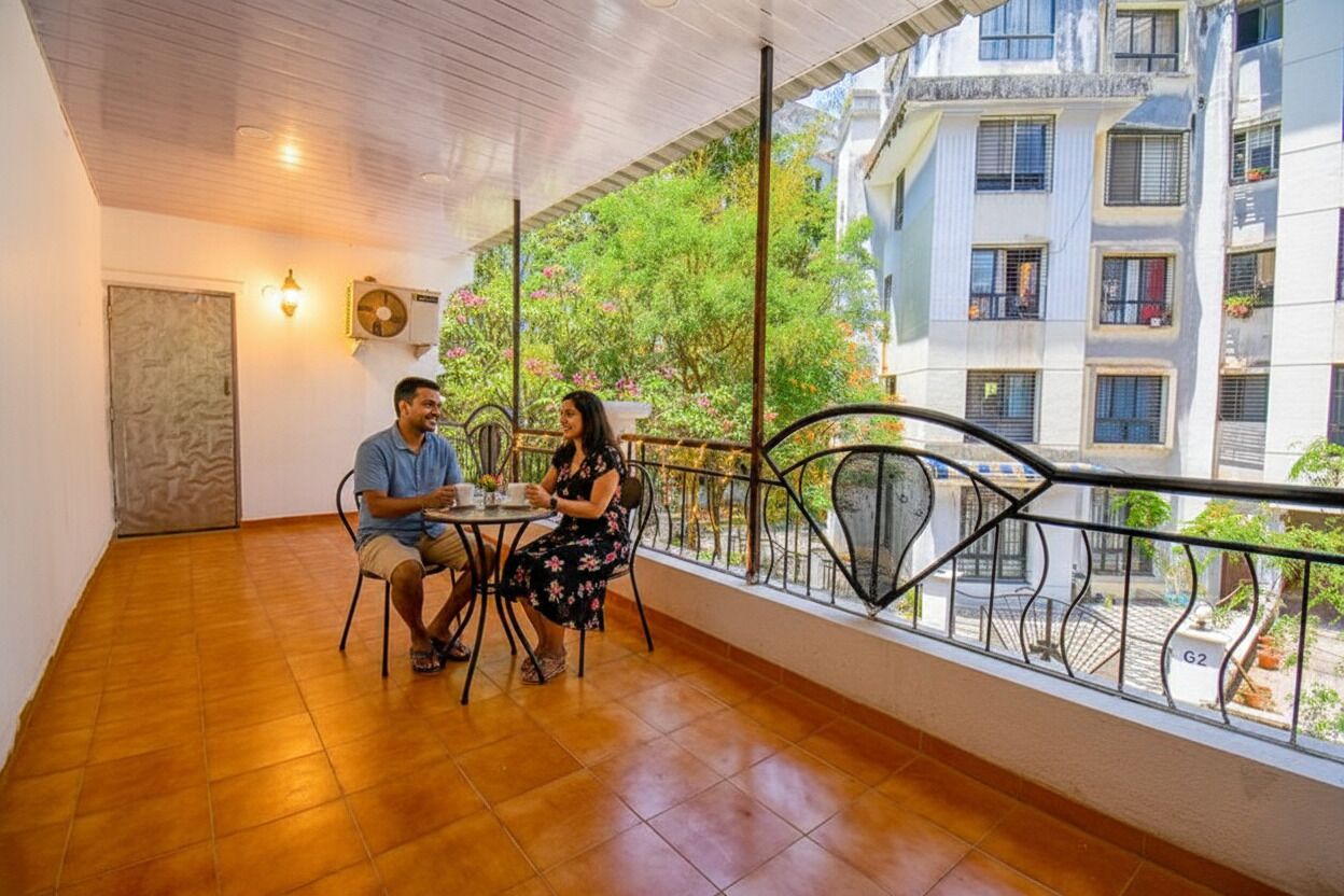 A balcony with a tiled floor and a railing, overlooking a residential area with buildings and greenery.