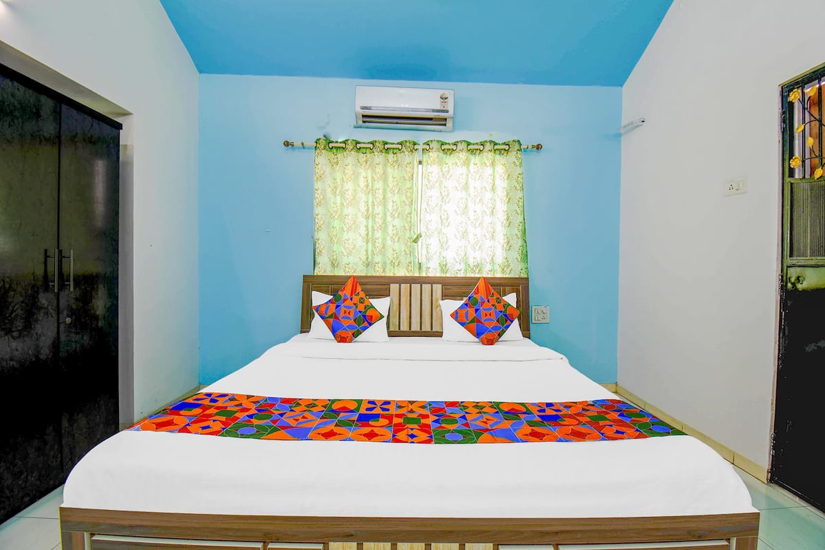 A bedroom with a bed, a window with curtains, an air conditioner, and a door.
