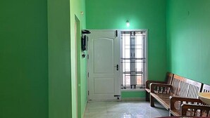 A room with green walls, a white door, a bench, and a window with bars. - FabExpress MK Homes (Kodaikanal)