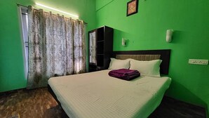 A room with a bed, a wardrobe, a mirror, and a green wall. - FabExpress MK Homes (Kodaikanal)