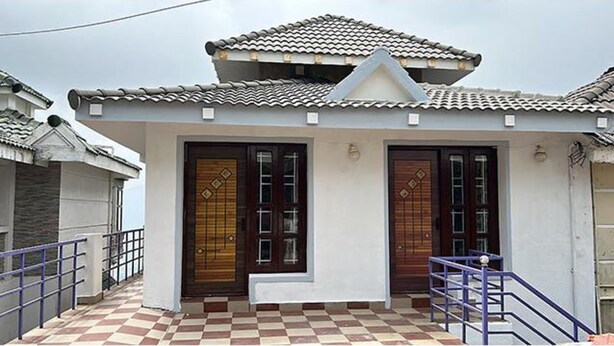 A two-story house with a tiled roof, two wooden doors, a checkered floor, and a small balcony with a railing. - FabExpress MK Homes (Kodaikanal)