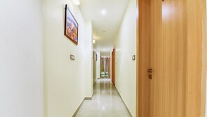 A hotel corridor with a wooden door on the right, a framed picture on the left, and a shiny tiled floor. - FabExpress Mewar Shine (Udaipur)