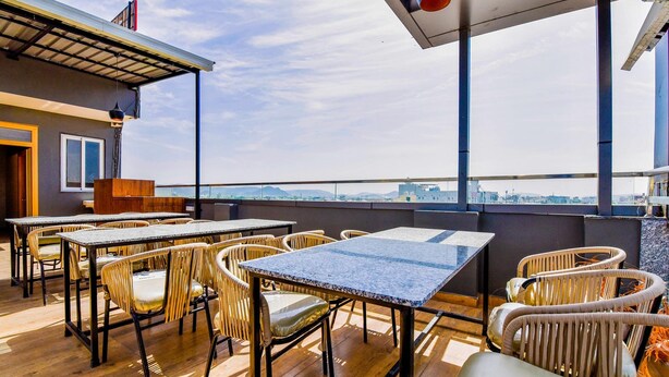 An outdoor terrace with tables and wicker chairs, overlooking a cityscape. - FabExpress Mewar Shine (Udaipur)