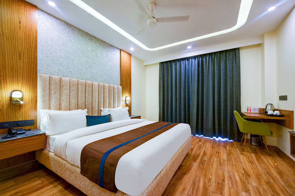A hotel room with a large bed, a desk with a chair, a ceiling fan, and a window with curtains.