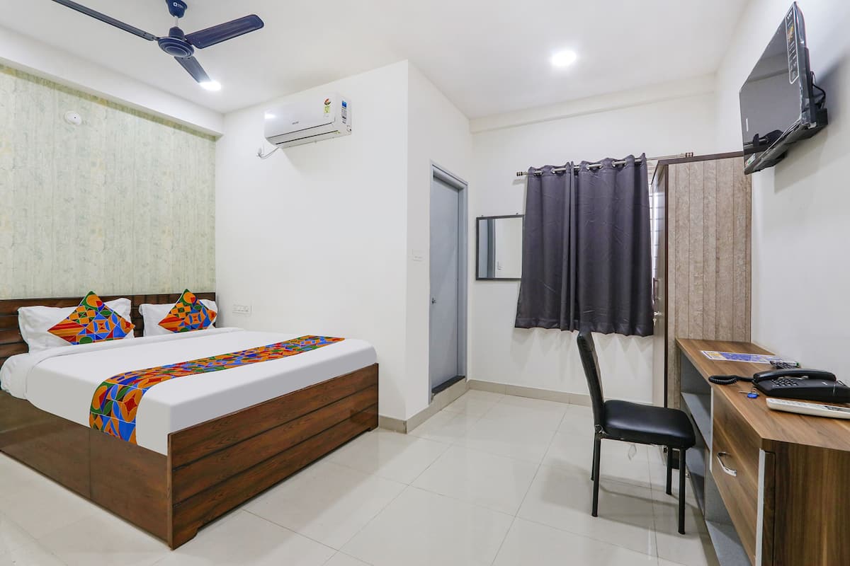 A bedroom with a bed, a desk, a chair, a TV, and an air conditioning unit.