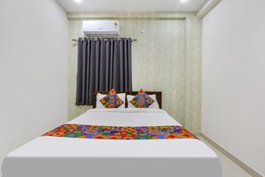 A neatly made bed with a colorful geometric-patterned bedspread, a headboard with decorative pillows, and an air conditioning unit mounted on the wall. - Via Dream Connect - Narsingi (Hyderabad)