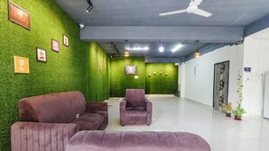 A room with green artificial grass walls, a ceiling fan, and a white floor. There are framed pictures on the wall and a few potted plants. - Via Dream Connect - Narsingi (Hyderabad)
