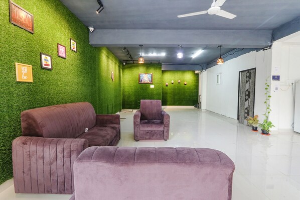 A room with green artificial grass walls, a ceiling fan, and a white floor. There are framed pictures on the wall and a few potted plants. - Via Dream Connect - Narsingi (Hyderabad)