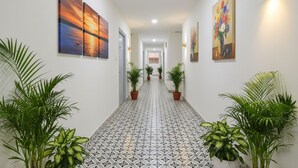 A hallway with patterned flooring, potted plants, and artwork on the walls. - Via Dream Connect - Narsingi (Hyderabad)