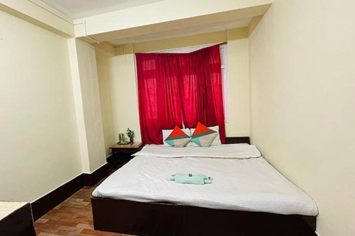 A small, neatly arranged bedroom with a bed, a nightstand, and a red curtain.