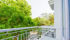 A balcony with white railings overlooking a lush green garden.