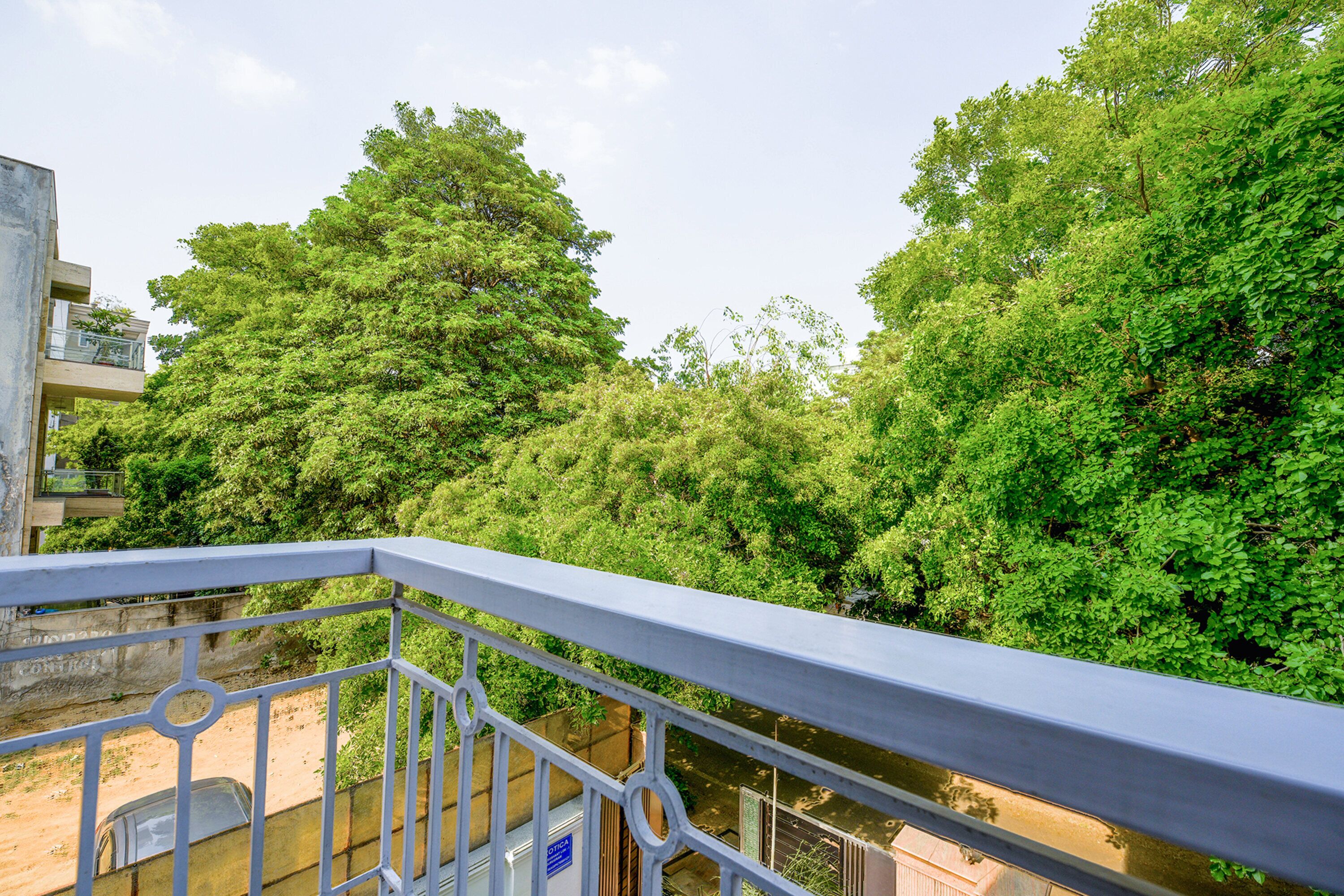 A balcony with a view of dense green trees and a building in the background.