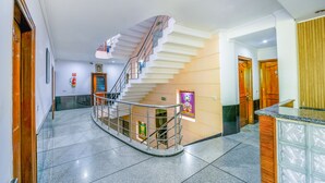 A modern hotel lobby with a curved staircase, a reception desk, and a tiled floor.