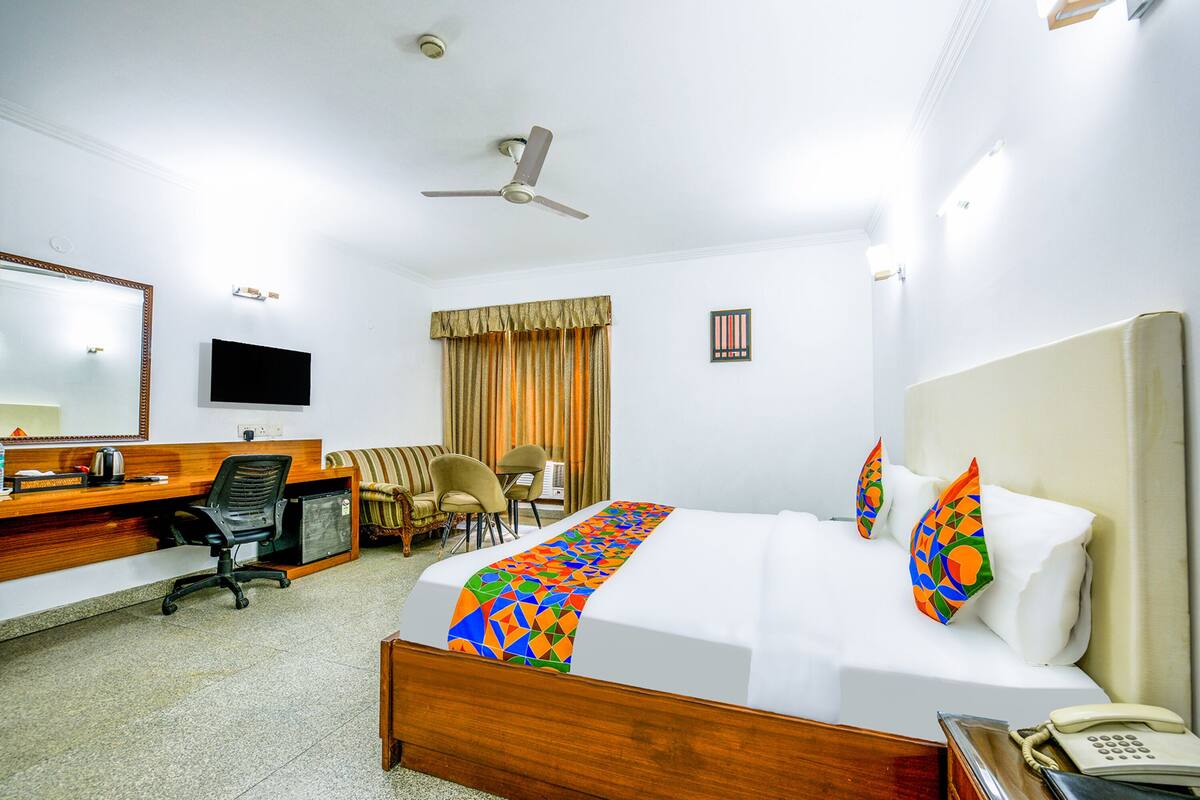 Habitación de hotel con cama, escritorio, sillas, televisor y teléfono.