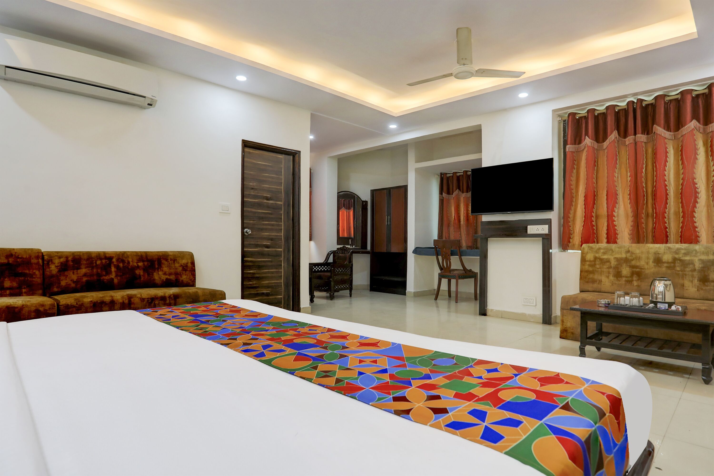 A hotel room with a large bed, a sofa, a TV, and a dining area.