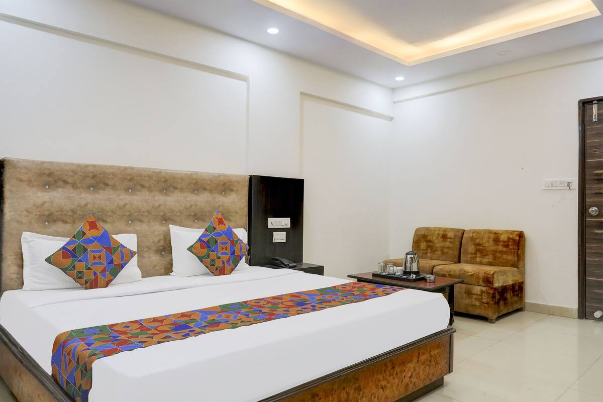 A hotel room with a large bed, a sofa, a nightstand, and a door.