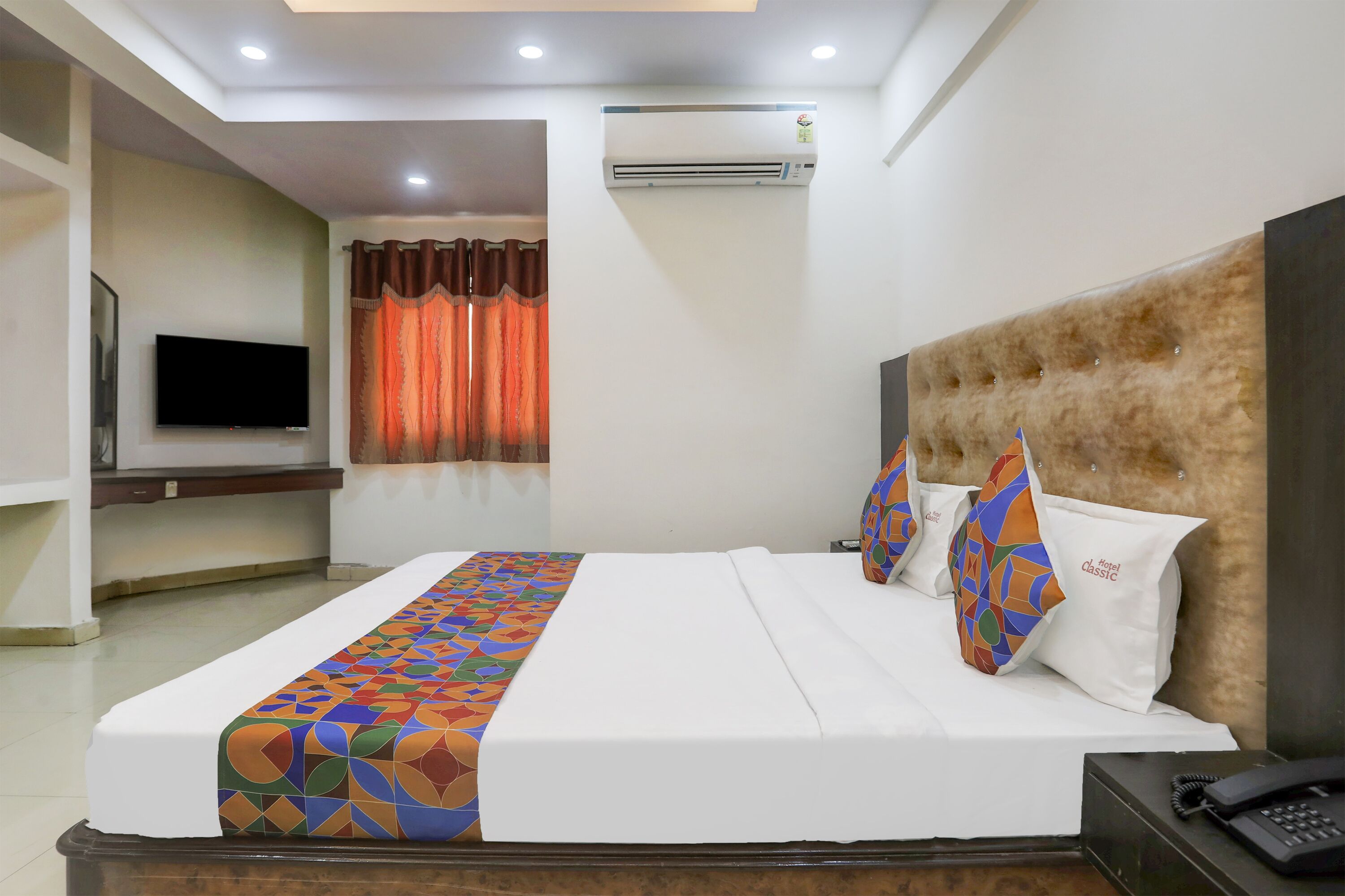 A hotel room with a bed, a TV, an air conditioner, and a telephone.