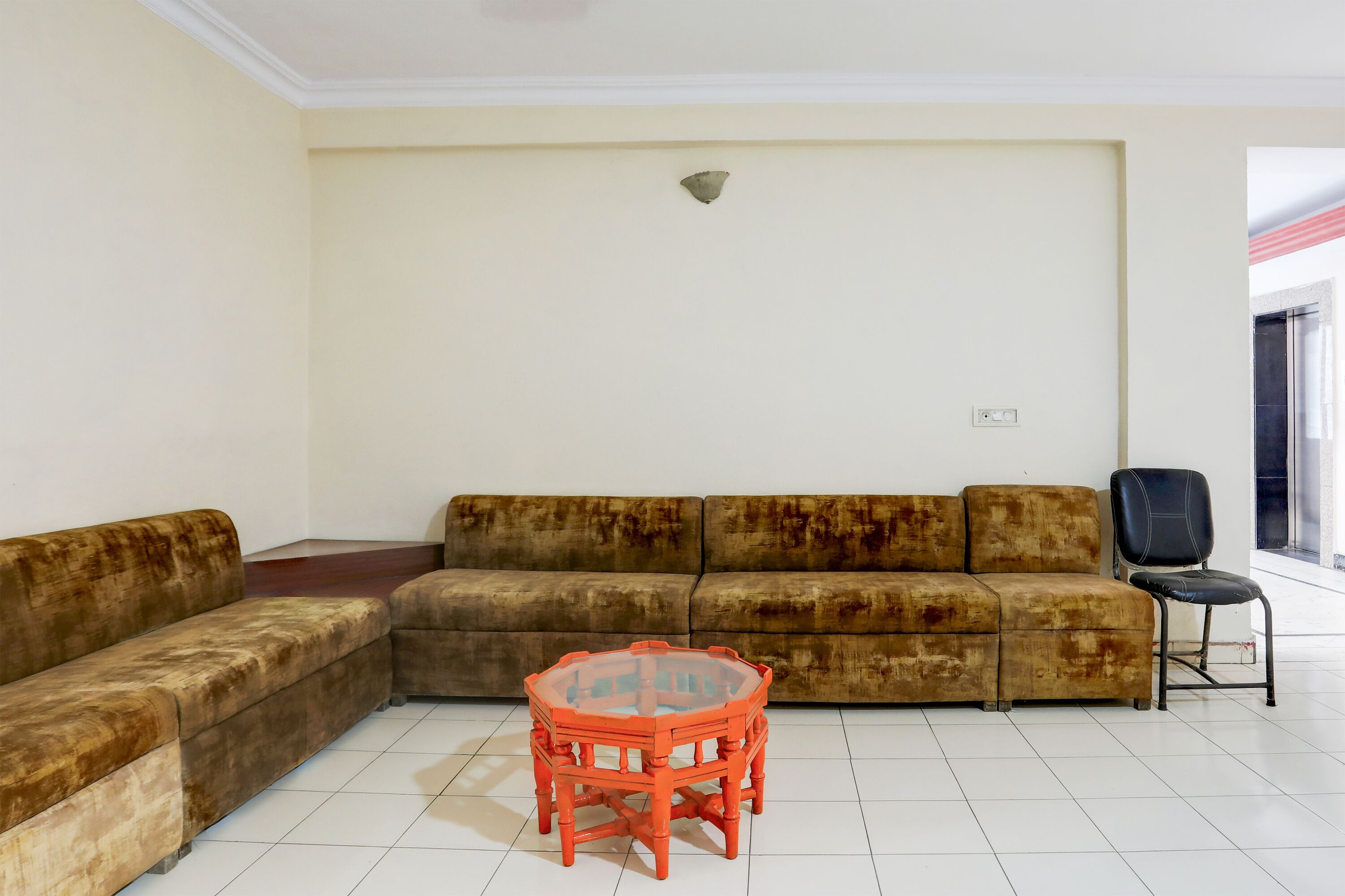 A living room with a brown sectional sofa, a red glass coffee table, and a black chair.