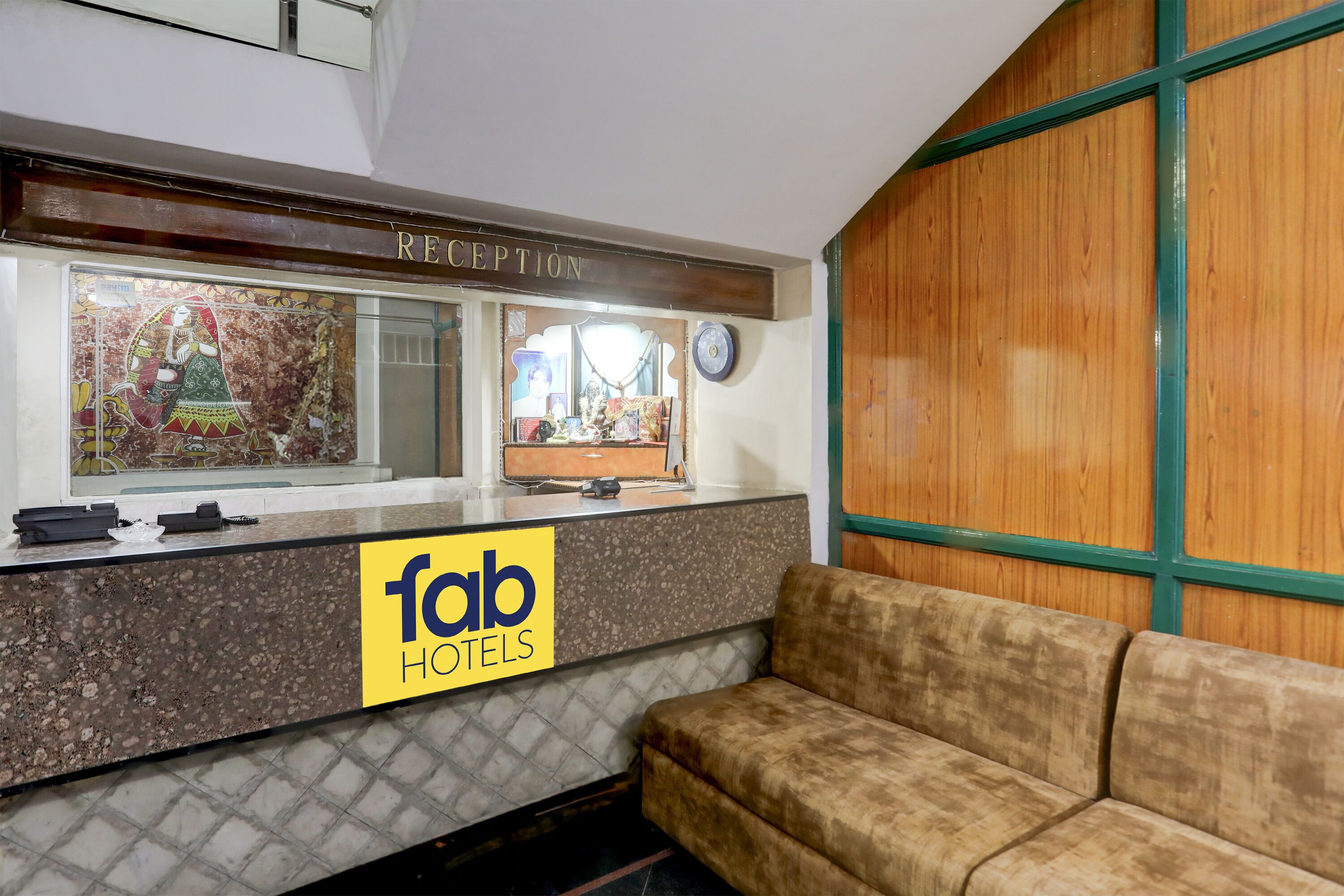 Un área de recepción con el letrero 'fab hotels', un mostrador de recepción, un sofá y una pared de madera.