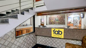 A reception area with a reception desk, a sign for 'fab hotels', a staircase, and a tiled floor. - FabHotel Classic (Bhopal)