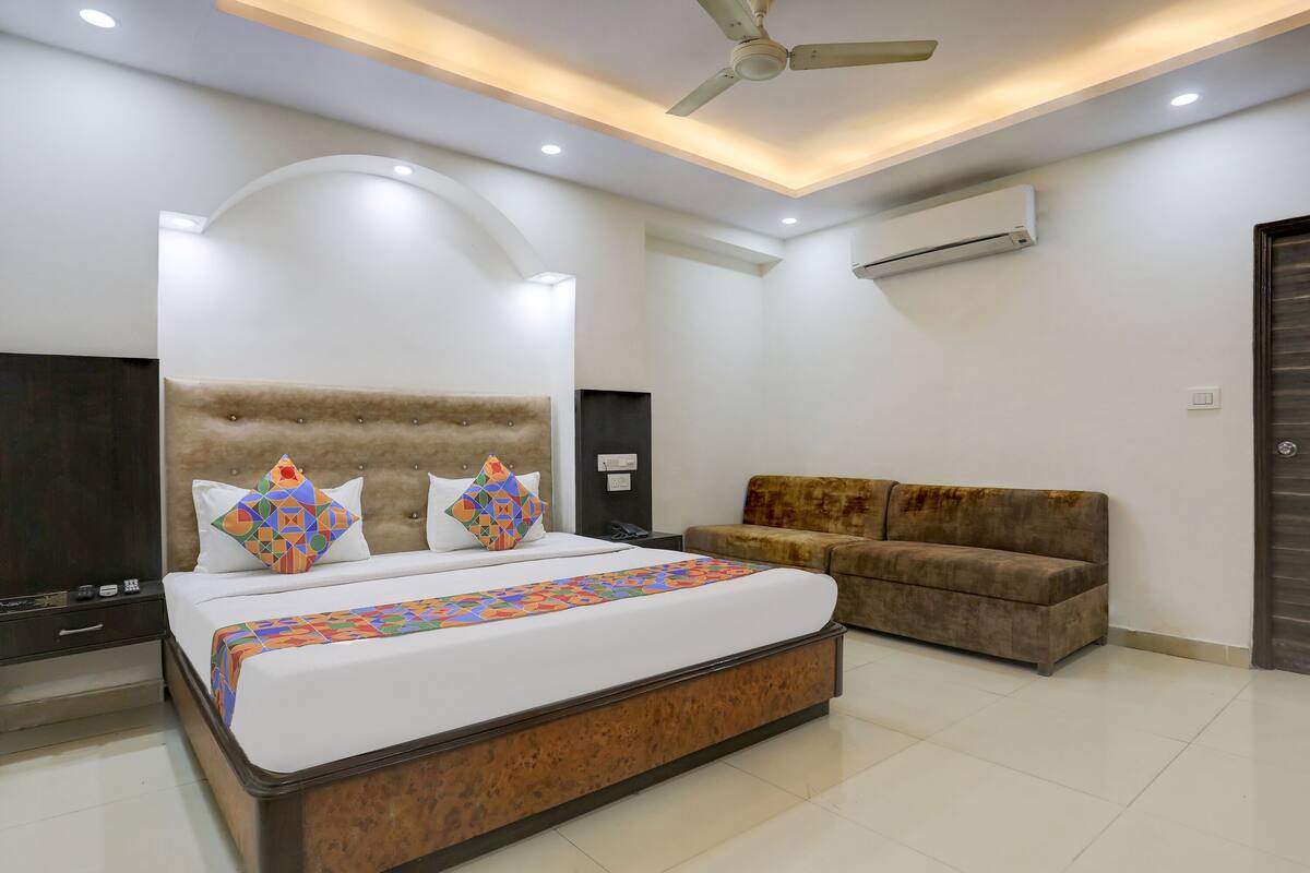 A modern bedroom with a large bed, a sofa, a ceiling fan, and an air conditioning unit.