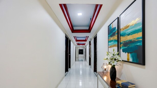 A modern hallway with a tiled floor, a wooden console table with books and a vase of flowers, and two framed artworks on the wall. - FabHotel Classic (Bhopal)
