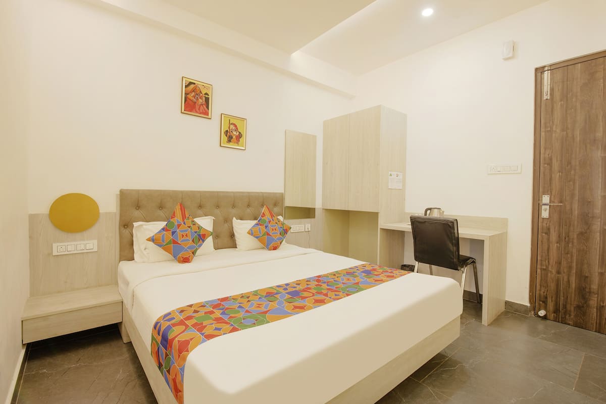 A hotel room with a bed, a desk, and a chair. There are two paintings on the wall.