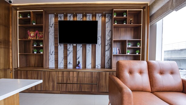 A modern living room with a wooden entertainment unit, a flat-screen TV, and a leather sofa. - FabHotel Silver Key (Anekal)