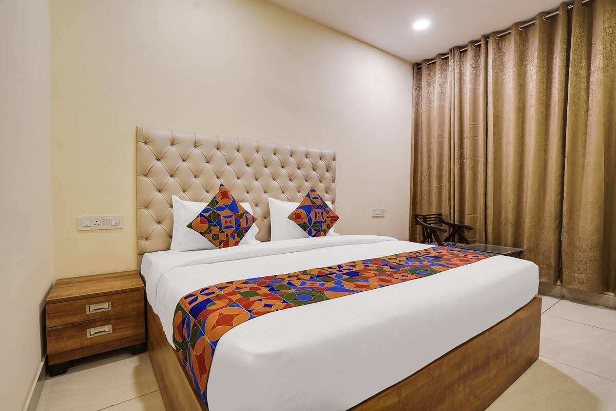 A neatly made bed with a patterned bedspread, a tufted headboard, and two pillows with geometric designs.