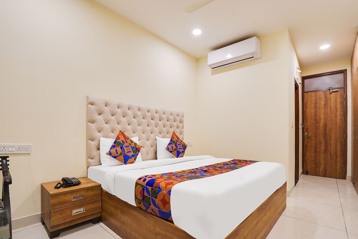 A neatly arranged bedroom with a tufted headboard, a bed with a colorful geometric-patterned bedspread, a bedside phone, and a wooden nightstand.
