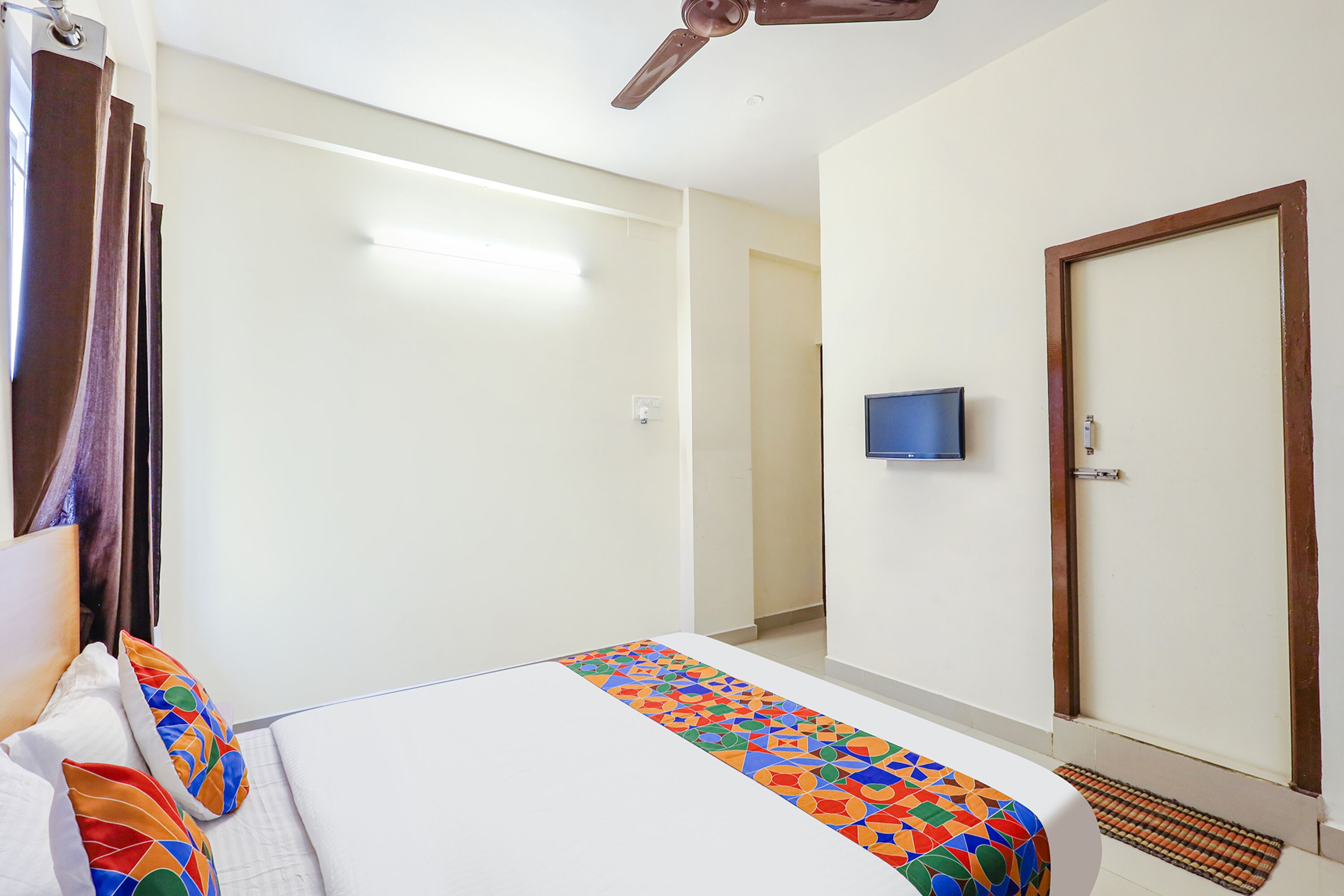 Una habitación de hotel con una cama, un ventilador de techo, un televisor en la pared y una puerta.
